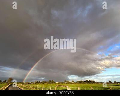 Uno splendido arco arcobaleno sopra campi lussureggianti sotto un cielo spettacolare, che mostra la vera bellezza della natura Foto Stock