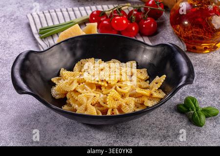 farfalle dorate in ciotola nera. Pomodori ciliegini rossi vivaci, basilico verde fresco, parmigiano salato, olio di peperoncino composizione completa Foto Stock