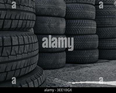 Pile di pneumatici invernali usati. Pile multiple di pneumatici neri per auto invernali con battistrada profondi, disposte in file su una superficie asfaltata presso il centro di assistenza pneumatici Foto Stock