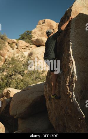 Uomo che bouldering su una parete rocciosa illuminata dal sole nel deserto della California Foto Stock