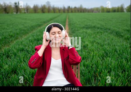 Donna in giacca rossa che ascolta musica con le cuffie sul campo Foto Stock