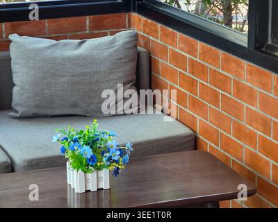 Angolo intimo caratterizzato da divano grigio contro pareti in mattoni rossi dietro un tavolo di legno scuro che regge un piccolo vaso di fiori blu a creare un'atmosfera tranquilla e rilassante Foto Stock