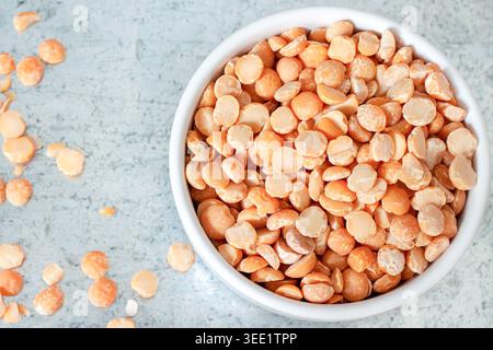 Ciotola bianca riempita con piselli crudi gialli secchi su fondo in lamiera grigia con grani sparsi Foto Stock