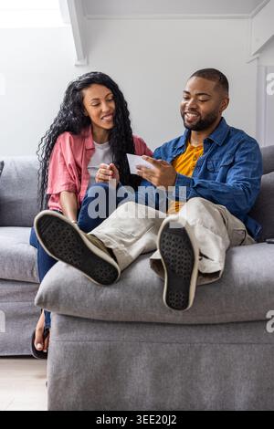 Diverse coppie sedute su un divano grigio nel soggiorno, tenendo in mano la carta stampata e mostrando le suole da sneaker Foto Stock