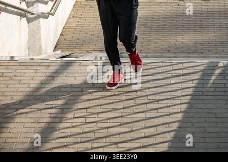 Red sneakers running on urban pavement with strong shadows during outdoor cardio training and active city lifestyle concept. Foto Stock