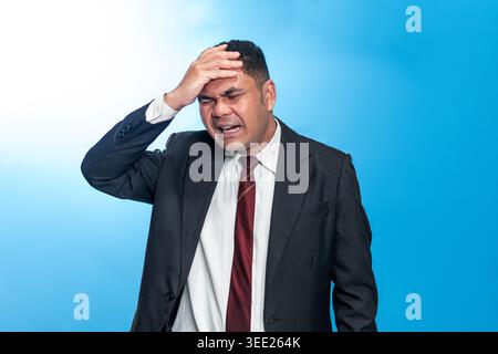 Ritratto di un uomo d'affari indonesiano con un vestito affetto da mal di testa o emicrania, toccando la fronte con un'espressione penosa e dolorosa. Foto Stock