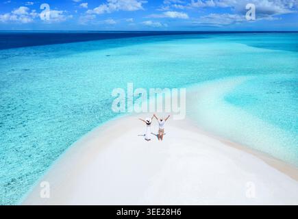 Vista aerea di una coppia felice in piedi su una spiaggia di sabbia con acque turchesi e cristalline nelle isole Maldive Foto Stock