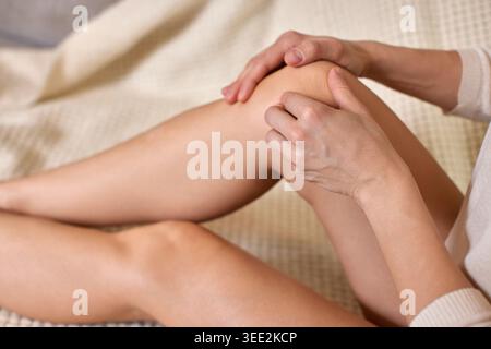 Donna che tocca e sfrega dolcemente il ginocchio, avverte disagio e dolore alle articolazioni della gamba, probabilmente a causa di lesioni o artrite Foto Stock