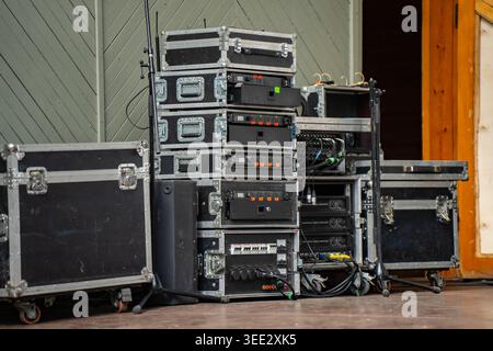 Apparecchiature audio professionali e custodie per rack audio sovrapposte su un palco all'aperto per un concerto dal vivo con amplificatori di potenza e microf wireless Foto Stock
