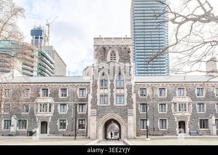 Vista frontale della Burwash Hall con arco centrale, finestre gotiche e facciata in pietra incorniciata da alti e moderni edifici. Foto Stock