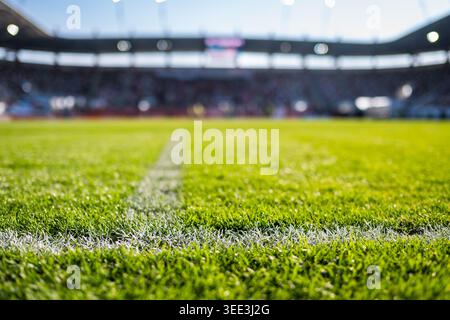 Vista ravvicinata ad angolo basso di una linea bianca di confine in gesso su un campo da calcio verde vivace con uno stadio sfocato sullo sfondo. Foto Stock