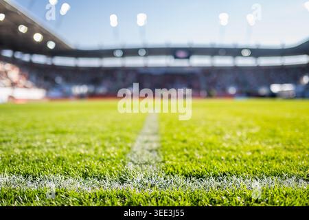 Vista ravvicinata ad angolo basso di una linea bianca di confine in gesso su un campo da calcio verde vivace con uno stadio sfocato sullo sfondo. Foto Stock