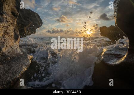 Vista delle onde oceaniche che si infrangono contro le scure rocce costiere sotto un'alba dorata in Florida, Stati Uniti. Foto Stock