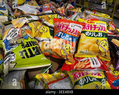 Un primo piano ad alto angolo di vari sacchetti di patate giapponesi Calbee impilati in un contenitore espositivo del supermercato. Foto Stock