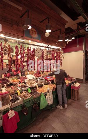 Uno stand al coperto a Firenze, in Italia, presenta una vasta gamma di frutta secca, frutta secca e spezie. Un fornitore, visto da dietro, meticolosamente ar Foto Stock