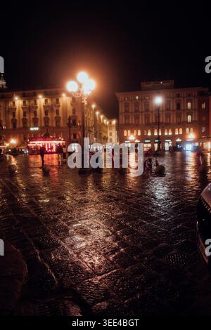 Una scena serale di strada a Firenze, in Italia, con pavimentazione bagnata di ciottoli che riflette il caldo bagliore dei lampioni e della finestra illuminata dell'edificio Foto Stock