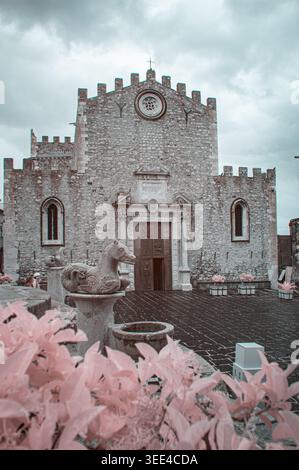 Una fotografia a infrarossi cattura la facciata in pietra grigia di un'antica chiesa di Taormina, Sicilia, Italia. Le sculture ornamentali adornano l'ingresso, fiancheggiate Foto Stock