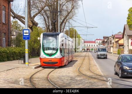 Mobilità vecchia e nuova - tram moderno che si avvicina lungo i binari acciottolati accanto agli edifici tradizionali e al traffico quotidiano a Liepaja, a dimostrazione della miscela Foto Stock