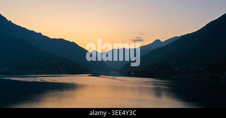 Tramonto estivo sul Lago di Ledro in Trentino, con riflessi calmi e sagome di montagna nei pressi della città di Ledro. Foto Stock