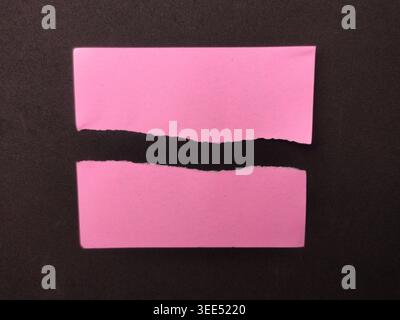 Un pezzo di carta rosa viene strappato orizzontalmente a metà, creando uno spazio scuro su uno sfondo nero. Foto Stock