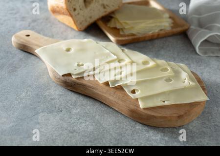 Una vista di diverse fette sottili di formaggio svizzero in stile americano, su un tagliere di formaggio di legno. Foto Stock