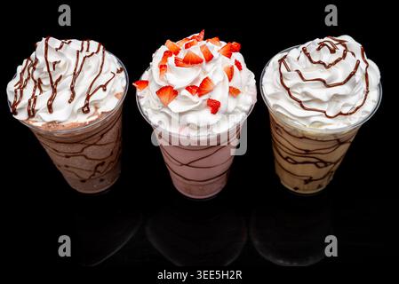 Tre frullati saporiti con panna, gocciolatoio di cioccolato e fette di fragola sopra di esso, pronti da bere. Foto Stock
