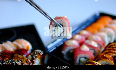 Sushi assortiti in vassoi di plastica nera con involtini di tonno conditi con maionese giapponese, mangiati con bacchette di legno e salsa di soia Foto Stock