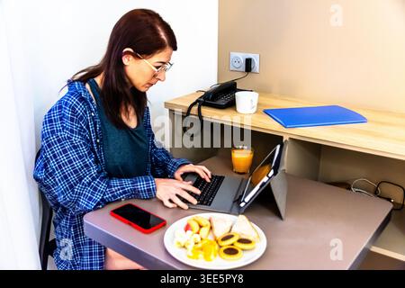 Donna che lavora in telelavoro mentre fa colazione in camera Foto Stock
