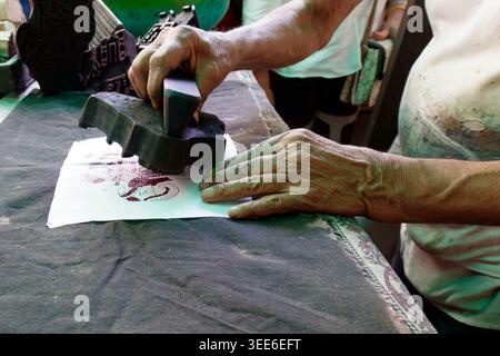 Primo piano di mani artigiane indiane utilizzando un blocco di batik in legno intagliato per stampare un motivo tradizionale sul tessuto Foto Stock