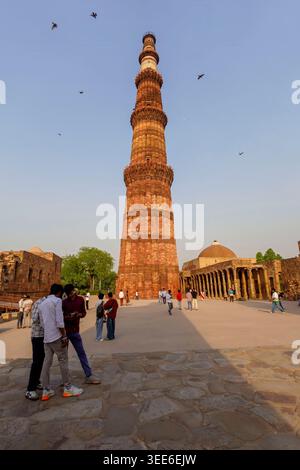 La torre della vittoria in pietra arenaria Qutub Minar e sito patrimonio dell'umanità dell'UNESCO a Delhi, India, con turisti che visitano l'antico complesso Foto Stock