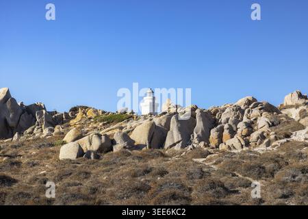 Vista del faro bianco di Capo testa, che si erge tra massicce formazioni rocciose di granito e macchia secca mediterranea sotto un cielo azzurro e limpido a Capo test Foto Stock
