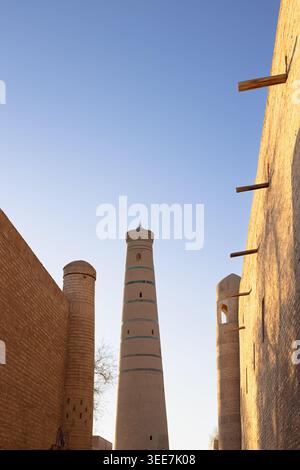 Minaret Islam Khodja con bande turchesi che si innalzano sopra le mura di mattoni di fango nella città vecchia di Khiva di Ichan Kala. Architettura storica islamica dell'Uzbekistan idaho Foto Stock