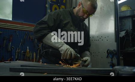 Operatore manuale qualificato che indossa dispositivi di protezione per la smerigliatura dell'acciaio in un'officina di saldatura. Concetto di carriera nell'industria metallurgica. Foto Stock