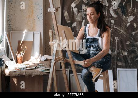 Hobby di artigianato e arte. Felice insegnante artistica in studio creativo con un look da cavalletto sulla sua immagine, godendo della creatività artigianale. copia spazio Foto Stock