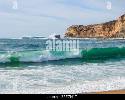 Vista panoramica con onde potenti e spiaggia di Silver Coast. Famoso faro di Nazare sulla ripida scogliera. Percorso di surf in Portogallo. L'oceano Atlantico tempestoso. Foto Stock