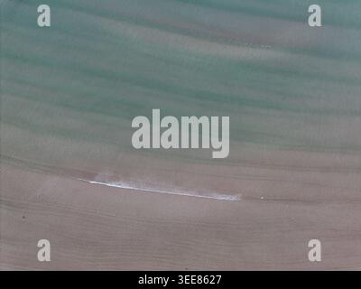 Vista aerea delle acque turchesi della baia di Gruinard, che incontrano la spiaggia sabbiosa con dolci increspature e una piccola onda a Gruinard, Scozia, Unite Foto Stock