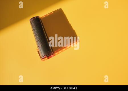 Striscia di pellicola con perforazioni che si srotolano su sfondo giallo, per mostrare il concetto di fotografia analogica Foto Stock