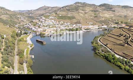 Vista aerea della città di Pinhao, annidata lungo il fiume Douro, con vigneti terrazzati su colline ondulate e barche da crociera attraccate sul lungomare Foto Stock