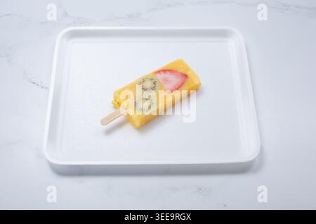 Una vista di una paleta di mango arancio ananas, con fette di kiwi e fragole. Foto Stock