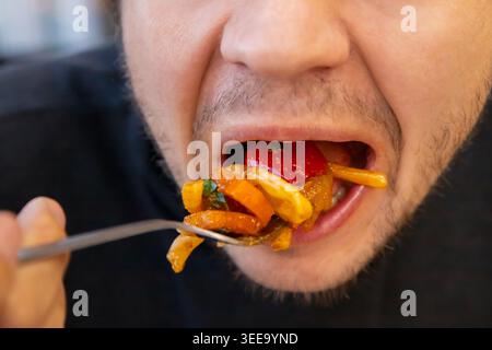 maschio che mangia una grande forkful di verdure fritte in padella con la bocca aperta, mostrando abitudini alimentari troppo alimentari e malsane. concetto di obesità, diabete Foto Stock