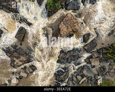 Veduta aerea delle cascate di Webuye con acqua marrone che precipita su grandi massi scuri e terreni rocciosi Webuye, Bungoma County, Kenya. Foto Stock