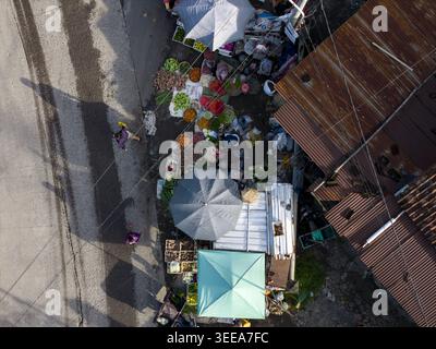 Vista aerea del mercato tradizionale di Pasar Kembang Klaten con bancarelle di verdure colorate, ombrelloni e persone che camminano lungo la strada accanto al campo arrugginito Foto Stock