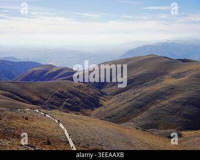 Un sentiero tortuoso si estende attraverso un vasto paesaggio montano con dolci picchi marroni e un orizzonte nebbioso sotto un cielo blu pallido vicino al Nemrut Dağ Foto Stock