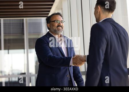 Due uomini d'affari sorridenti che stringono la mano nell'ufficio della compagnia Foto Stock