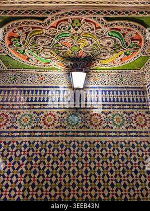 Piastrelle ornate in ceramica e soffitto intagliato illuminati da una lampada all'interno dello snack rack Café Riad nella vecchia Medina, 8 agosto 2025, Fez, Marocco Foto Stock