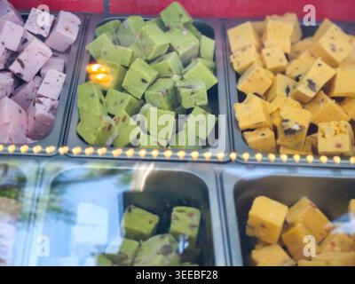 Colorato assortimento di dolci tradizionali indiani esposti in una cassa di vetro, con varietà rosa, verde e giallo con forme distinte e. Foto Stock