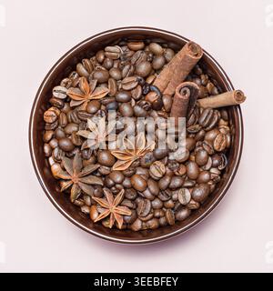 Caffè in chicchi tostati con cannella, anice stellato in tazza in ceramica marrone su sfondo rosa quadrato macro Foto Stock