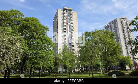 Due alti edifici residenziali in cemento con ripetitivi balconi sfalsati sorgono dietro un lussureggiante parco cittadino caratterizzato da prati verdi e fiorite primaverili Foto Stock