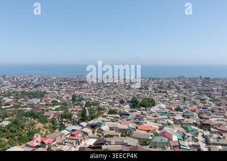 Ampia vista panoramica sulla città di Derbent, con fitti tetti residenziali, strade e vegetazione che si estende fino all'orizzonte del Mar Caspio, Daghestan, Russia Foto Stock