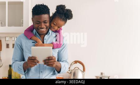 Padre e figlia condividono un momento insieme mentre usano un tablet in cucina Foto Stock